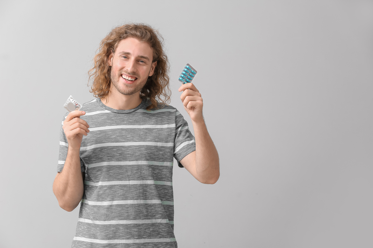 Young Man With Oral Erectile Dysfunction Medication And Condom On Grey Background ¿Qué Debo Hacer Para Cuidar La Glándula Prostática?